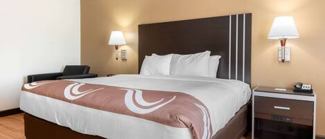 A hotel room with a large bed, bedside tables, and wall-mounted lamps.
