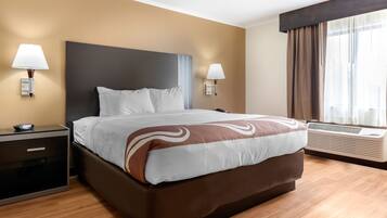 A hotel room with a large bed, bedside lamps, a nightstand, a window with curtains, and an air conditioning unit.