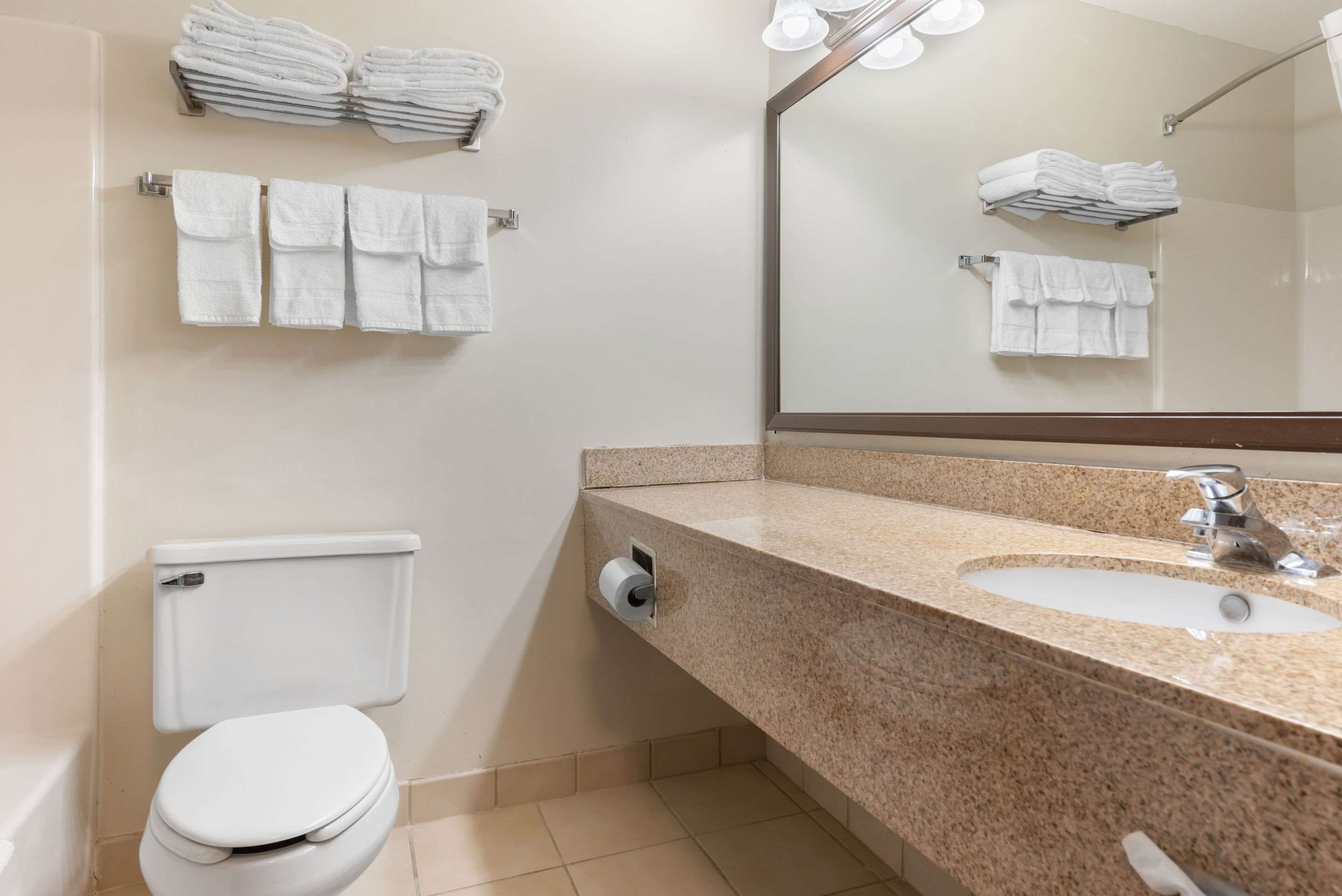 A bathroom with a toilet, sink, and stacked towels on shelves.