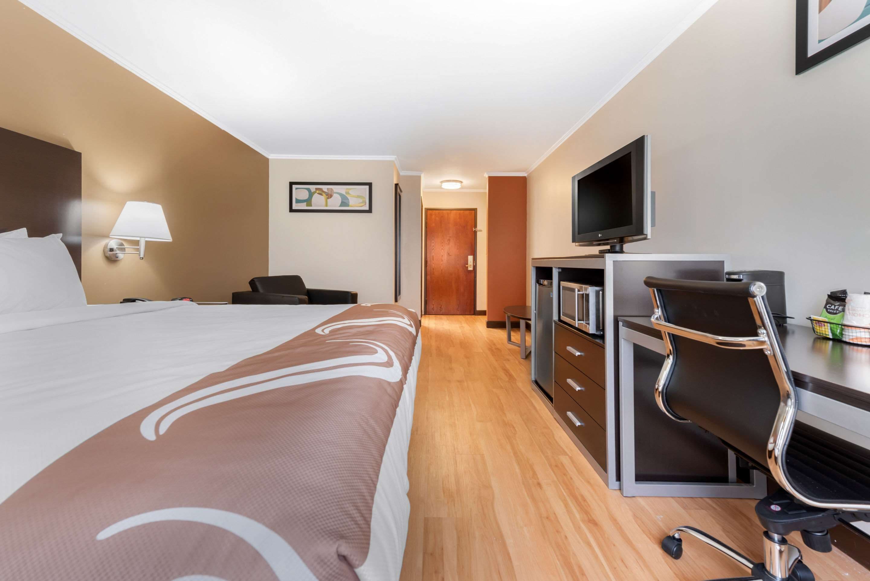 Ein Hotelzimmer mit einem großen Bett, einem Schreibtisch mit Stuhl, einem Fernseher und einer Minibar.