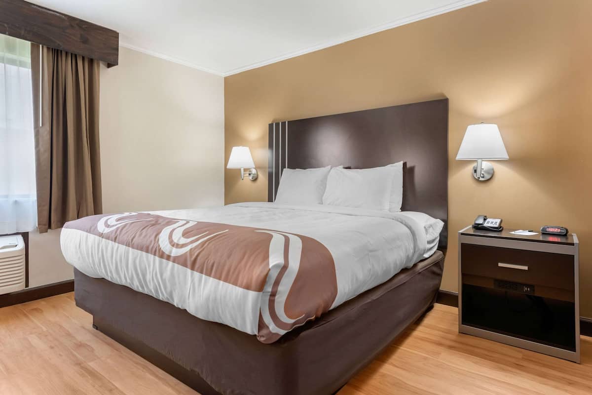 A hotel room with a large bed, two bedside tables with lamps, and a wooden floor.