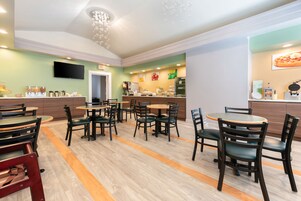Un restaurante con varias mesas y sillas, una zona de cocina y un televisor colgado en la pared.