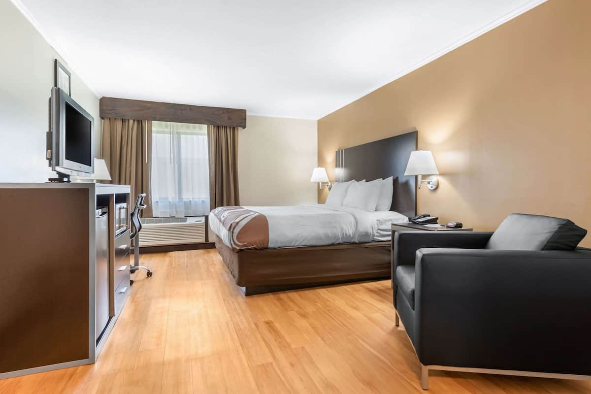 A hotel room with a bed, a desk with a computer, a TV, a chair, and a window with curtains.