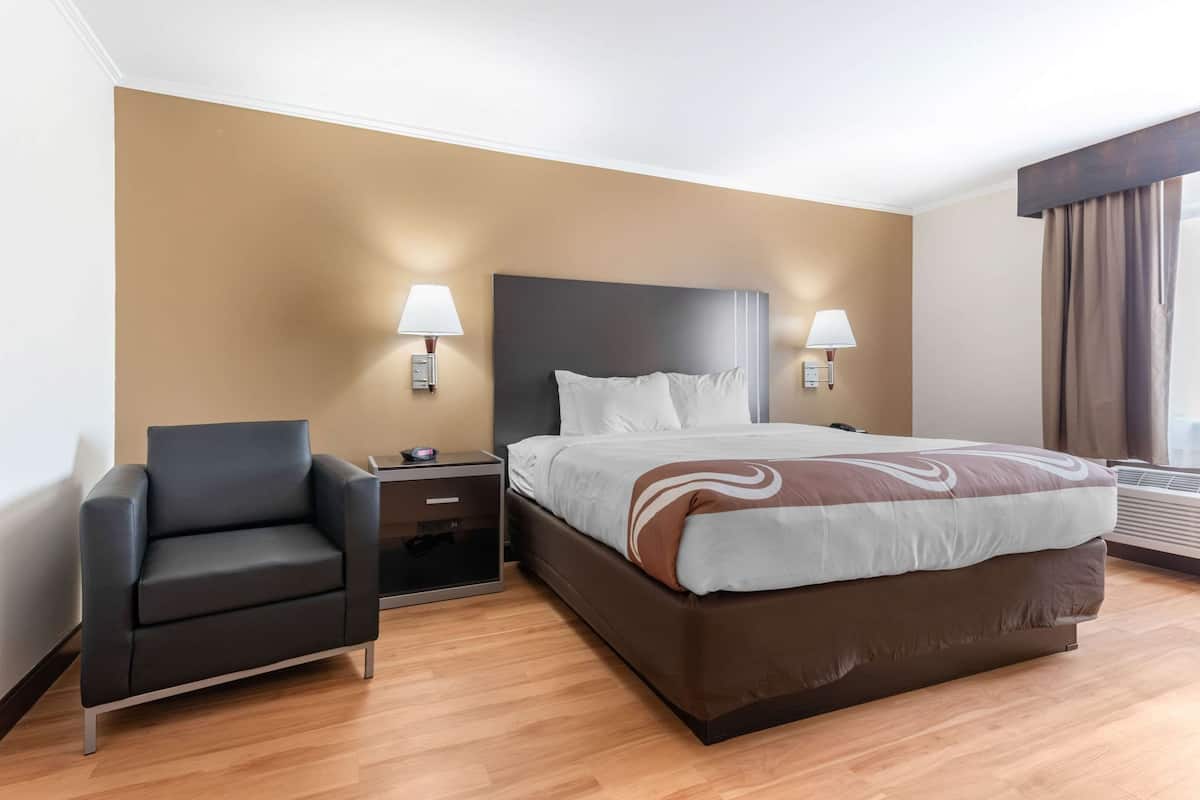 A hotel room with a bed, a chair, bedside tables, lamps, and a window with curtains.