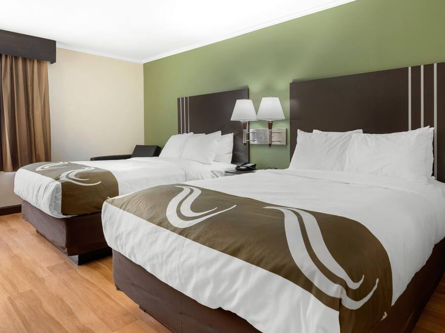 Habitación de hotel con dos camas, una mesita de noche, una lámpara y una ventana con cortinas.