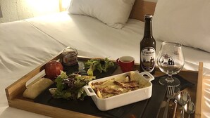 Bandeja de desayuno en una cama con una botella de vino, una copa y una ensalada.