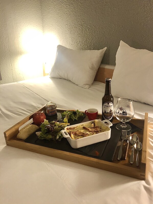 A breakfast tray on a bed with a bottle of wine, a glass, and a salad. - ibis Chartres Ouest Luce (Lucé)