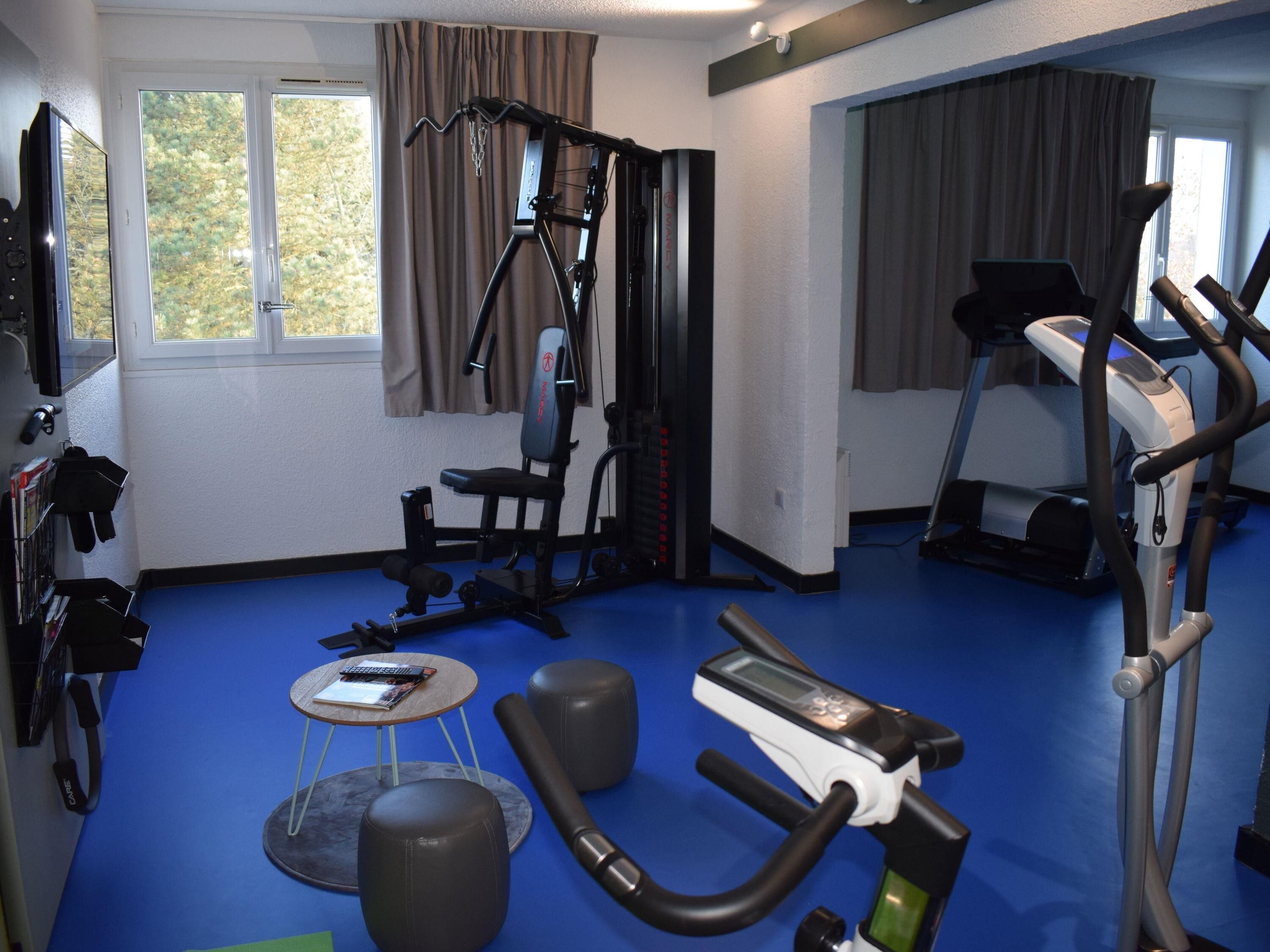 A fitness room with exercise equipment, a treadmill, and a window with curtains.