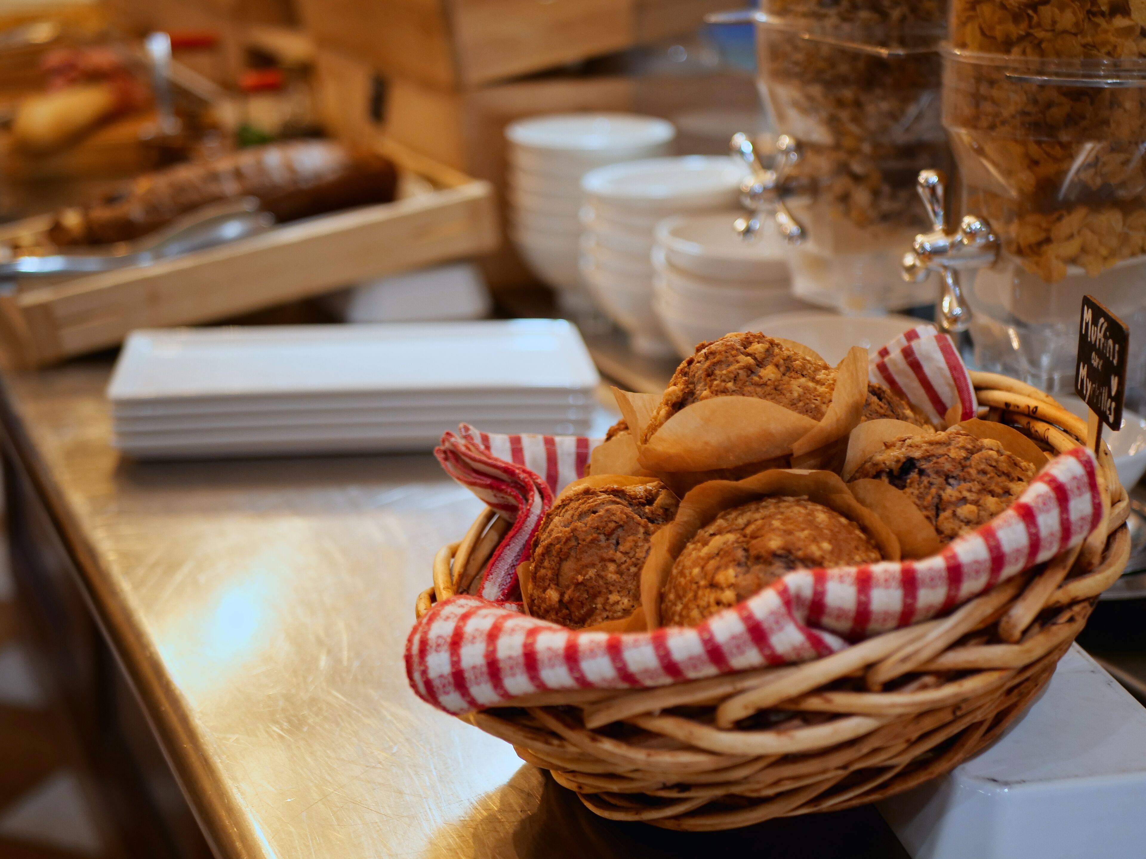 En bakke med kager på et buffetbord med hvide tallerkener og en kaffemaskine i baggrunden.