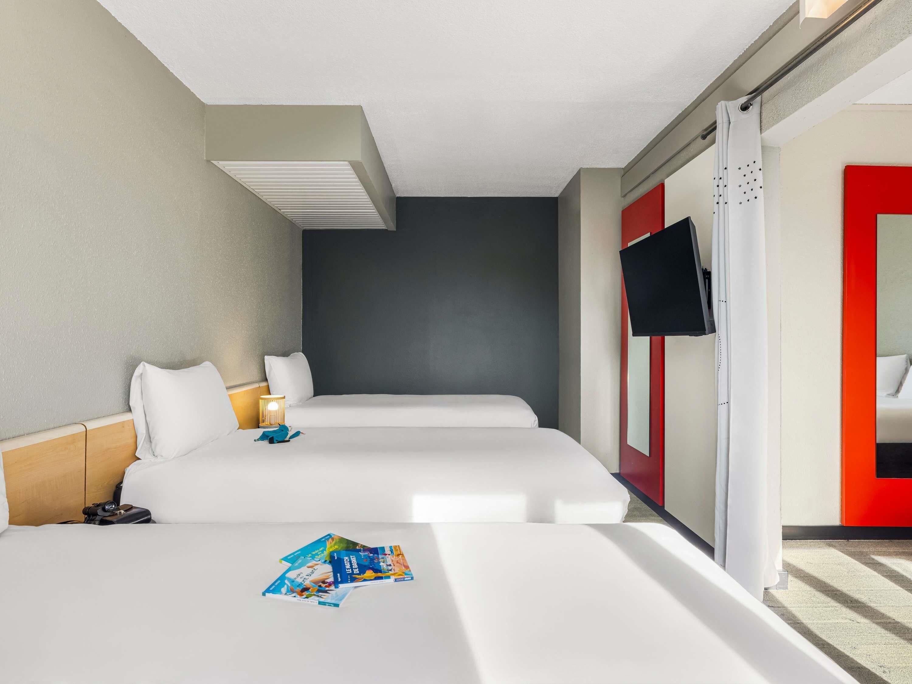 A hotel room with two beds, a television, and a red accent wall.