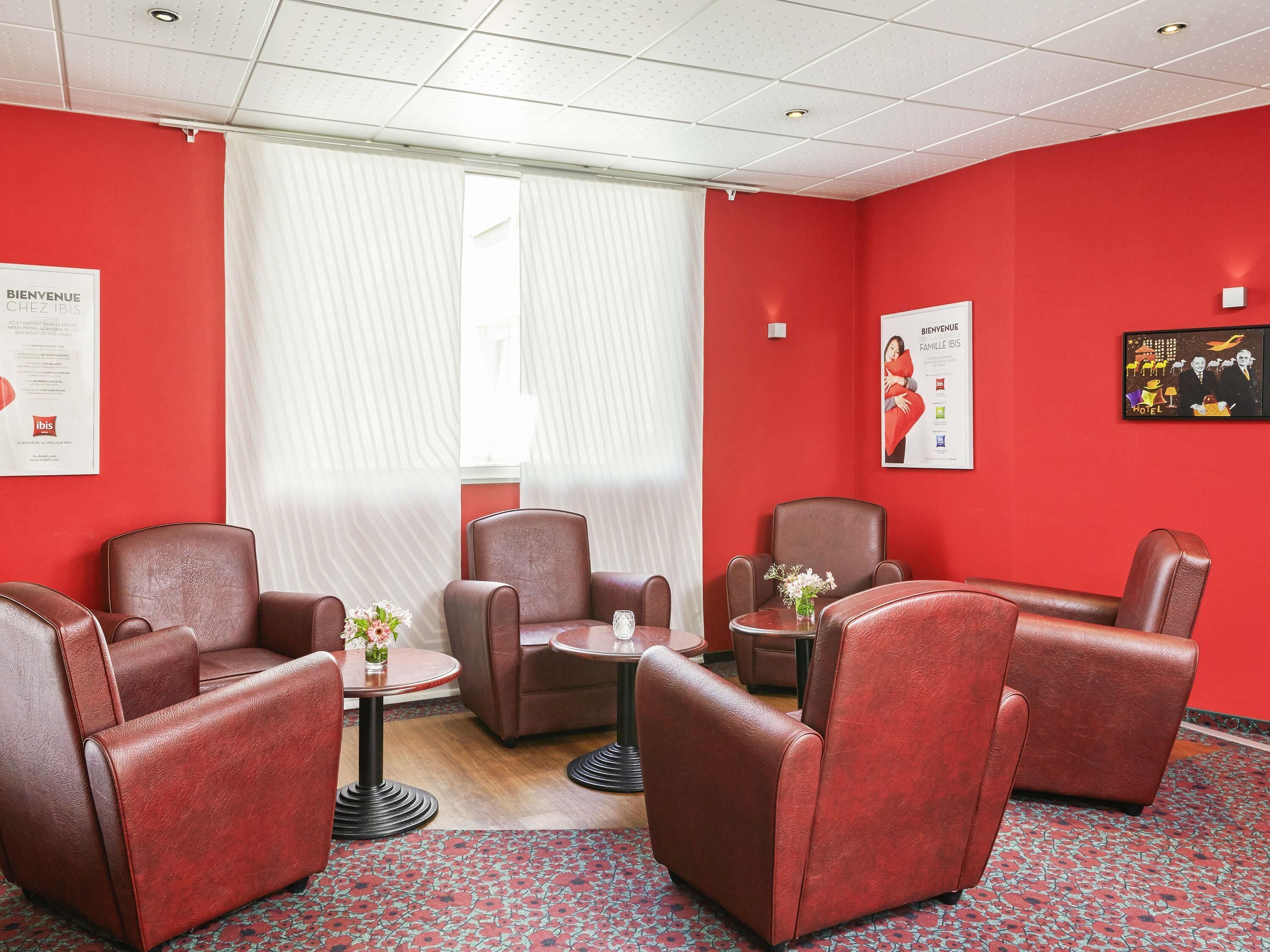 A hotel room with red walls, leather armchairs, a small table with a vase, and a window with blinds.