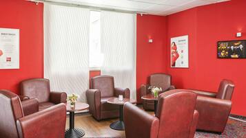 A hotel room with red walls, leather armchairs, a small table with a vase, and a window with blinds.