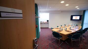 A conference room with a long table, chairs, a TV screen, and a sign indicating the room's name and capacity.