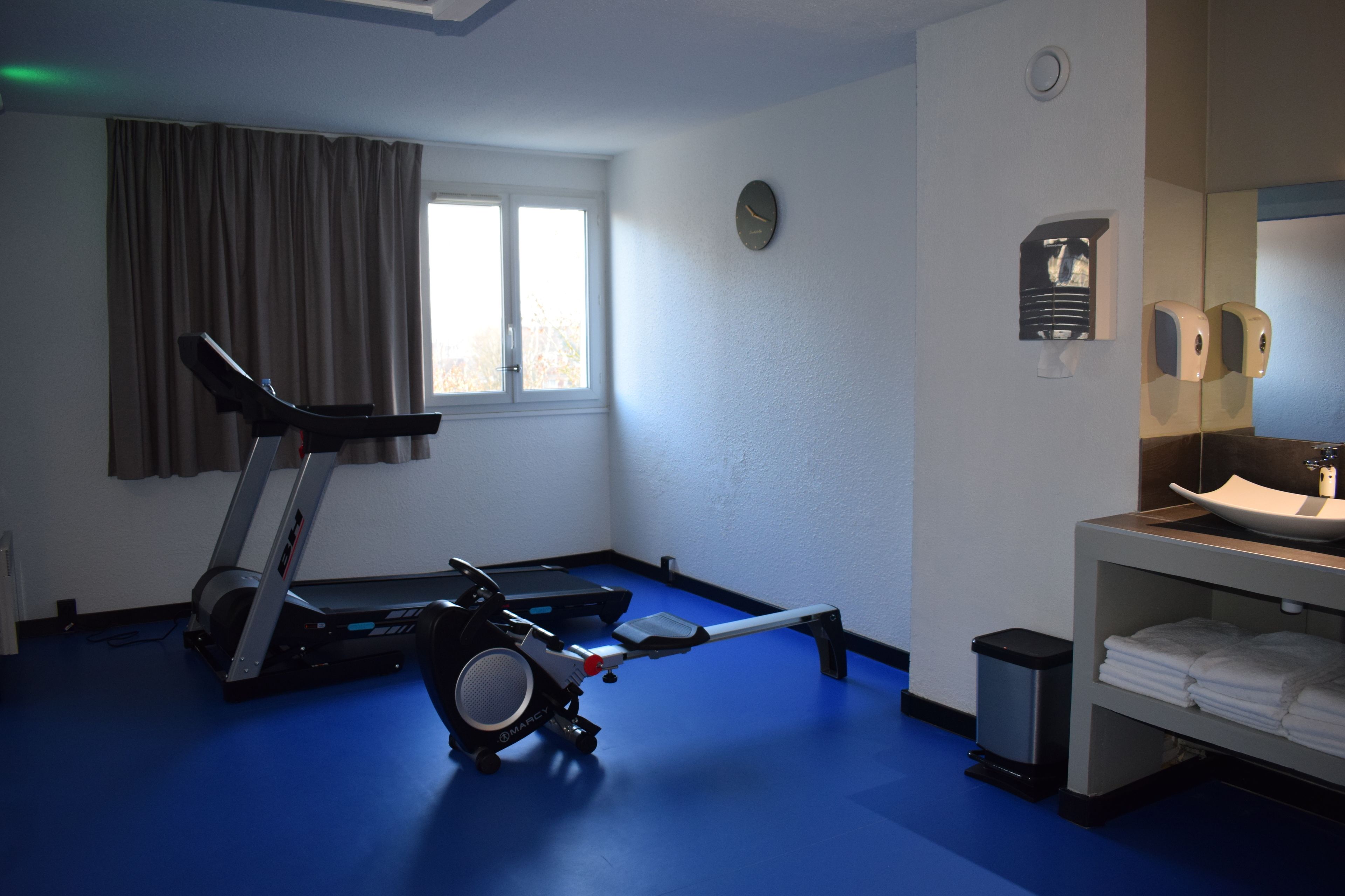 A room with a treadmill, exercise bike, and a small trash bin.