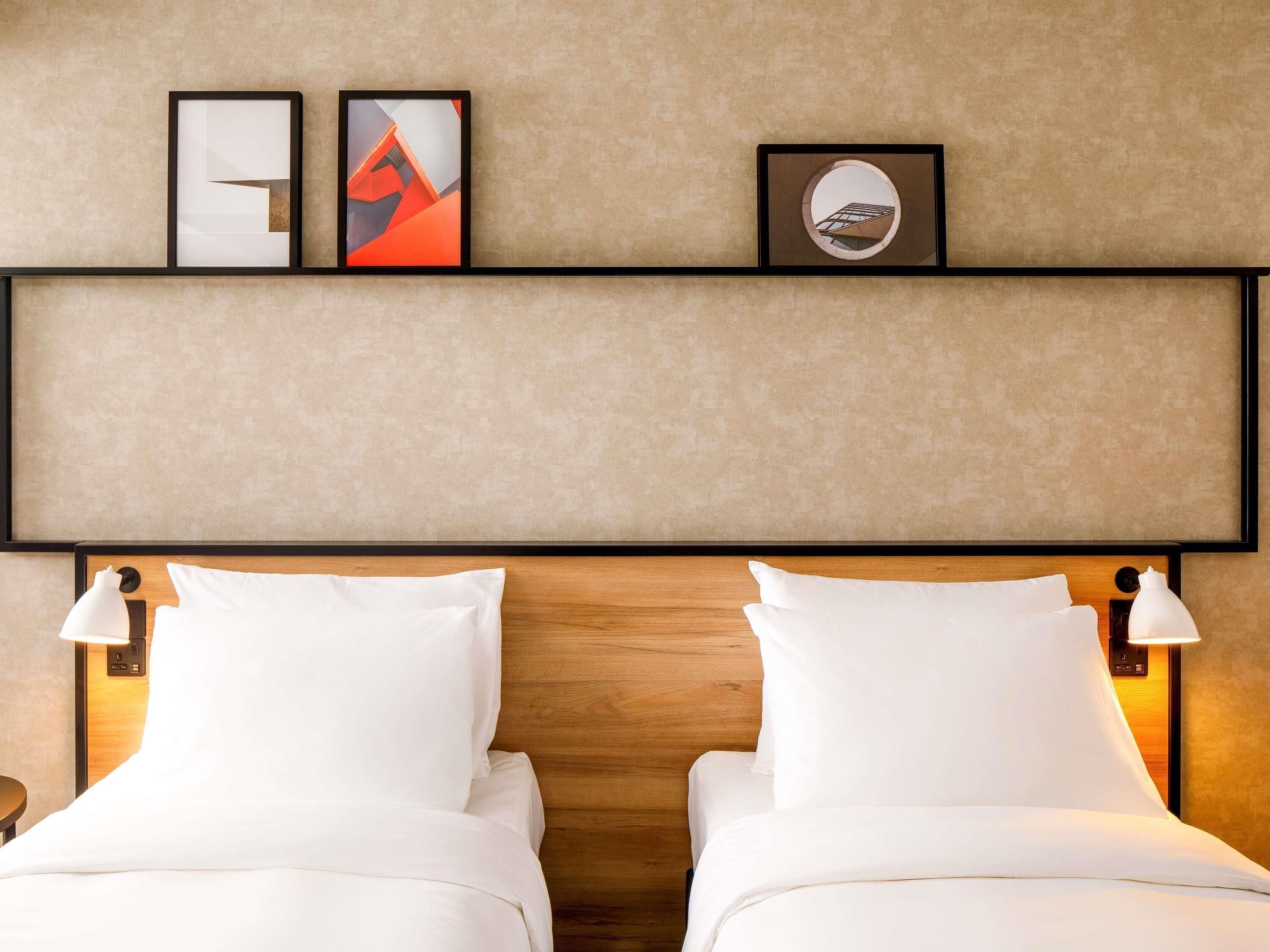 A hotel room with two beds, a wooden headboard, wall-mounted artwork, and bedside lamps.