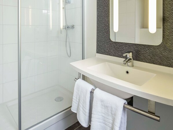 A modern bathroom with a glass shower enclosure, a white sink with a mirror, and a towel rack.