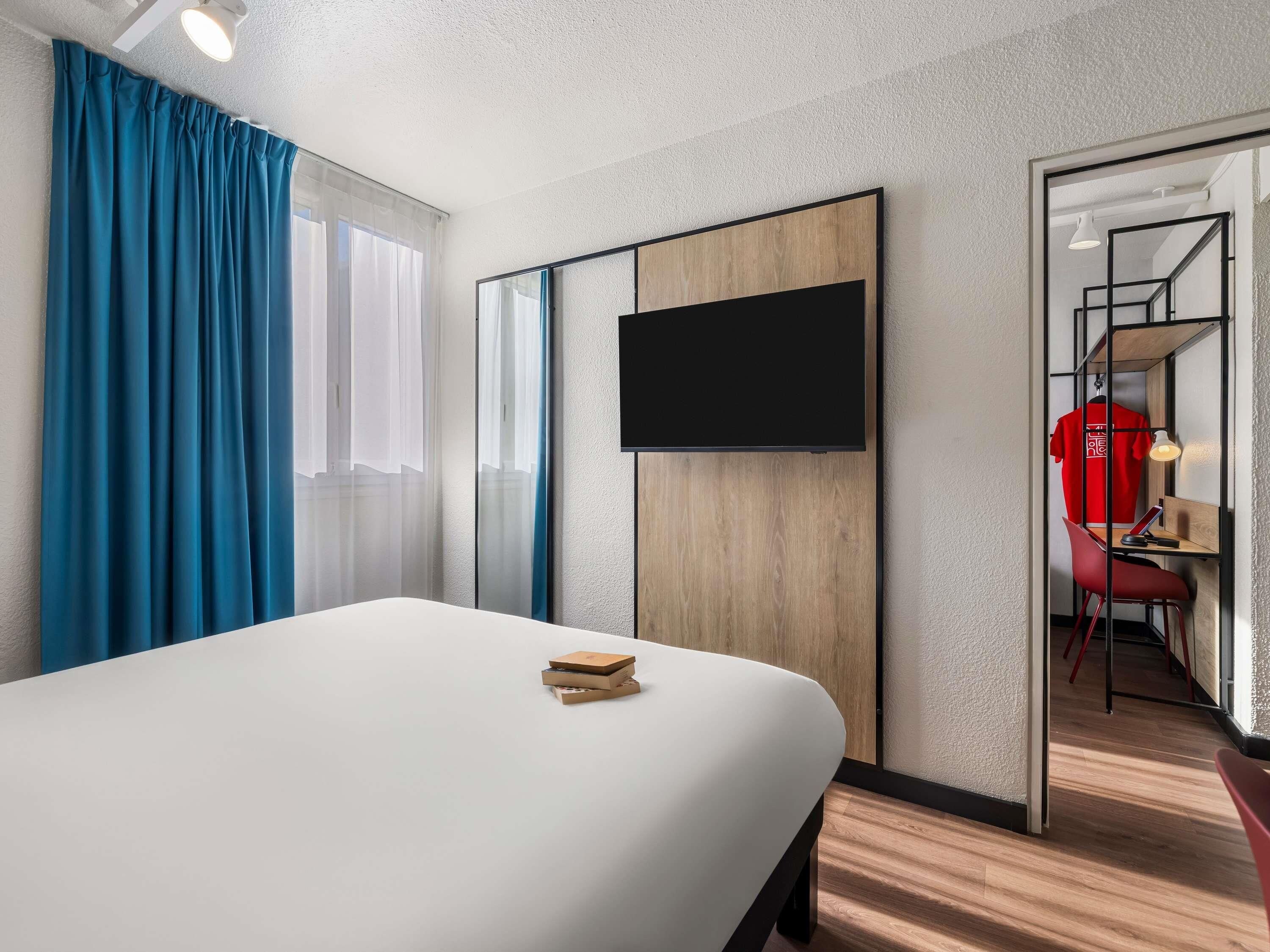 Habitación de hotel con cama, televisor montado en la pared, escritorio con silla y armario.