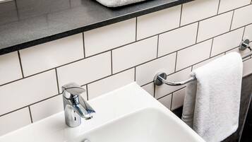 Une salle de bain avec un lavabo blanc, un robinet chromé et un porte-serviettes sur lequel est posée une serviette blanche.