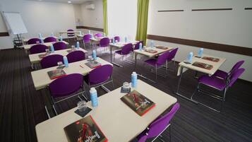 Ein Konferenzraum mit mehreren Tischen und violetten Stühlen, ausgestattet mit Wasserflaschen und Namensschildern.
