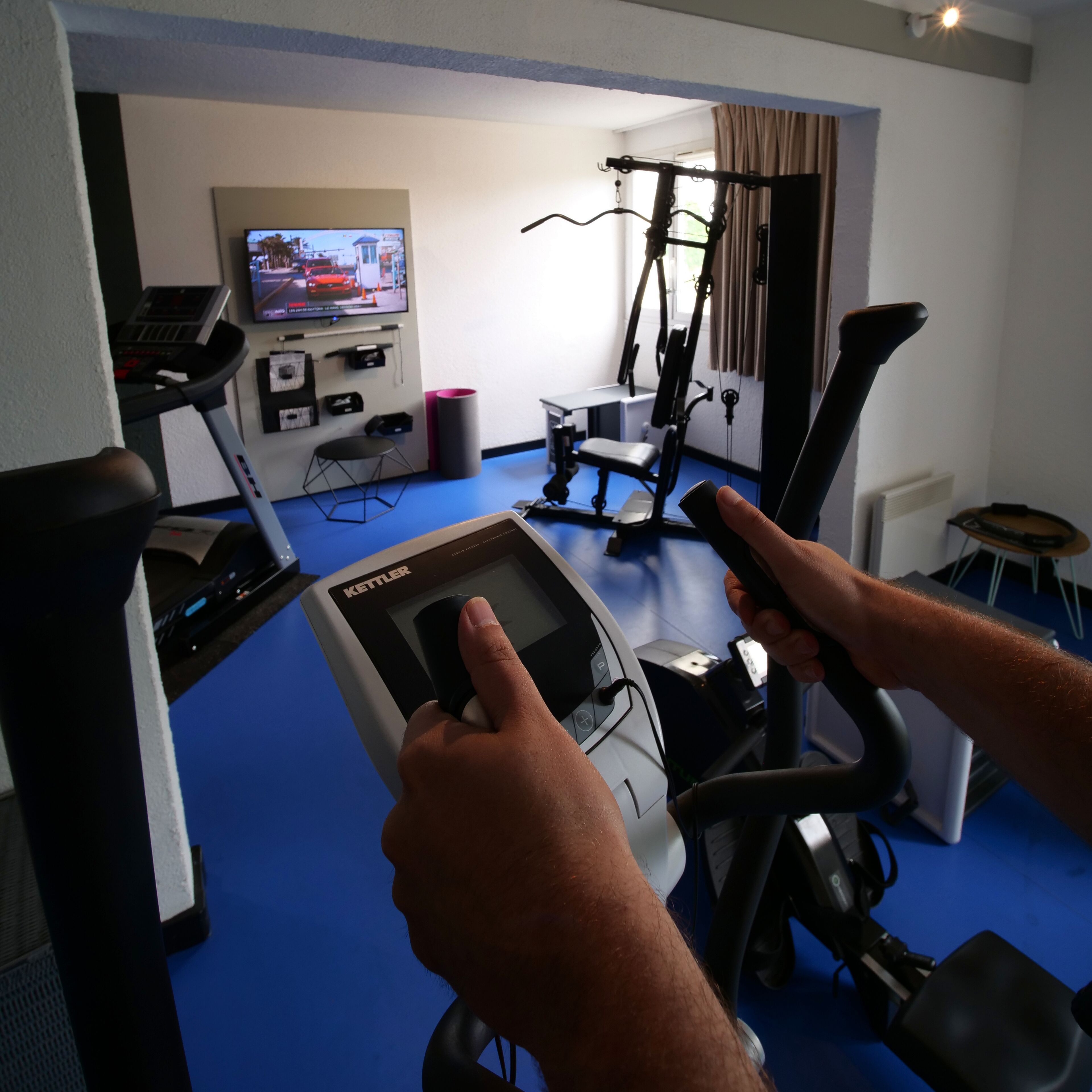 A home gym with exercise equipment, a treadmill, and a television displaying a program.