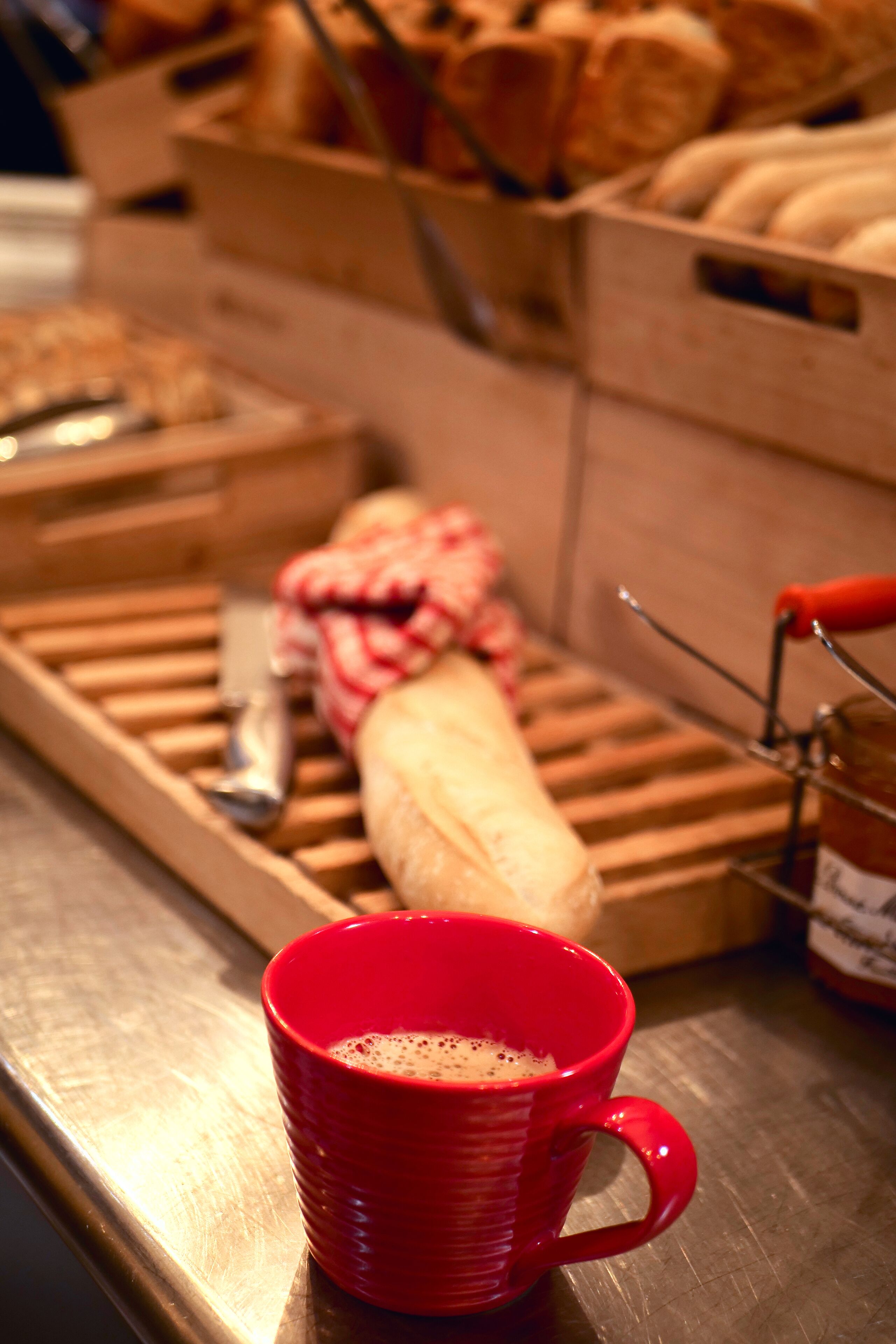 A breakfast setup with bread, a baguette, and a red mug on a tray.
