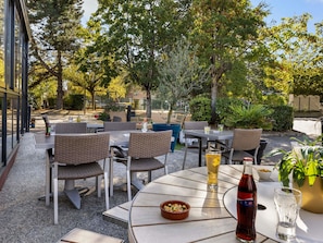 An outdoor patio with round tables and wicker chairs, surrounded by trees and greenery. - ibis Chartres Ouest Luce (Lucé)