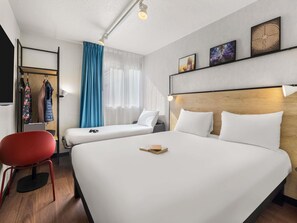 Habitación de hotel con dos camas, una silla roja, un cabecero de madera y un estante con obras de arte.