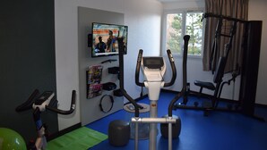 Un gimnasio con equipamiento de ejercicio, un televisor y una ventana con cortinas.