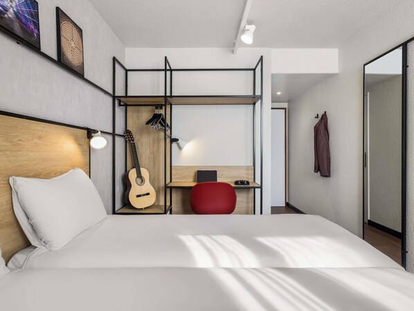 Una habitación de hotel moderna con cama, una guitarra, un escritorio y una silla roja.