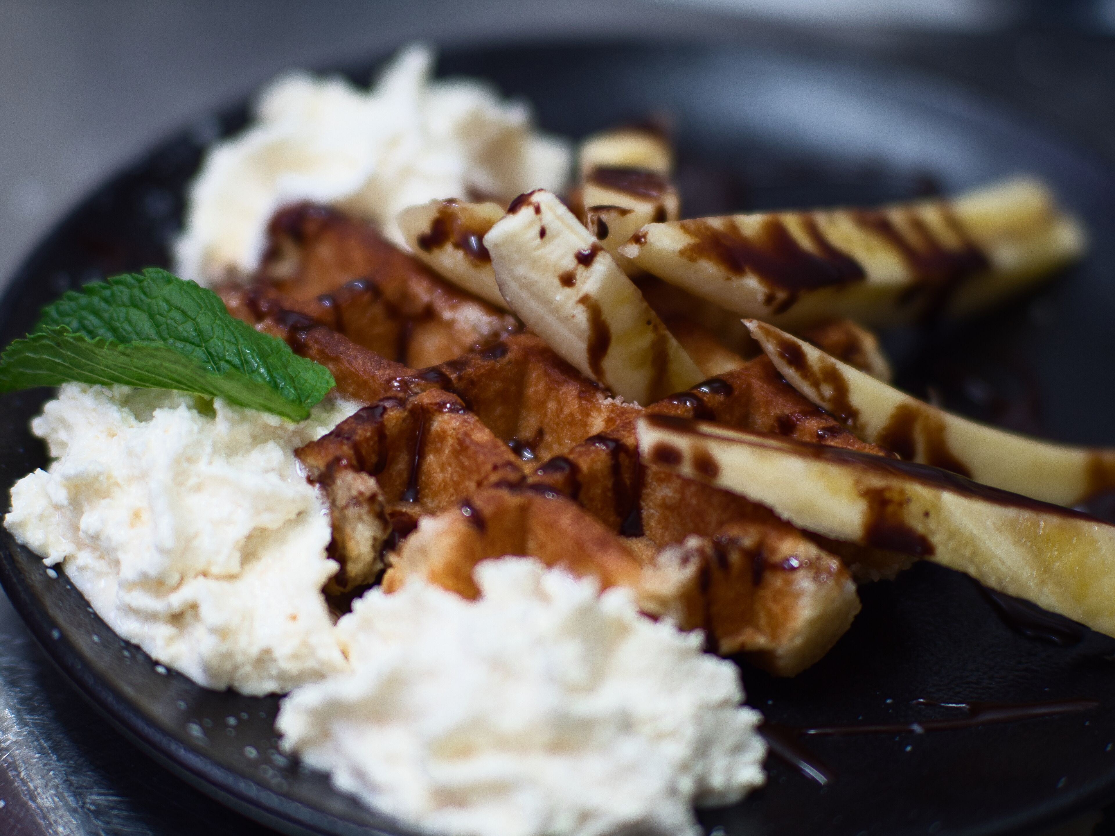 Ein Teller mit Waffeln, Bananenscheiben, Schlagsahne und einem Minzblatt.