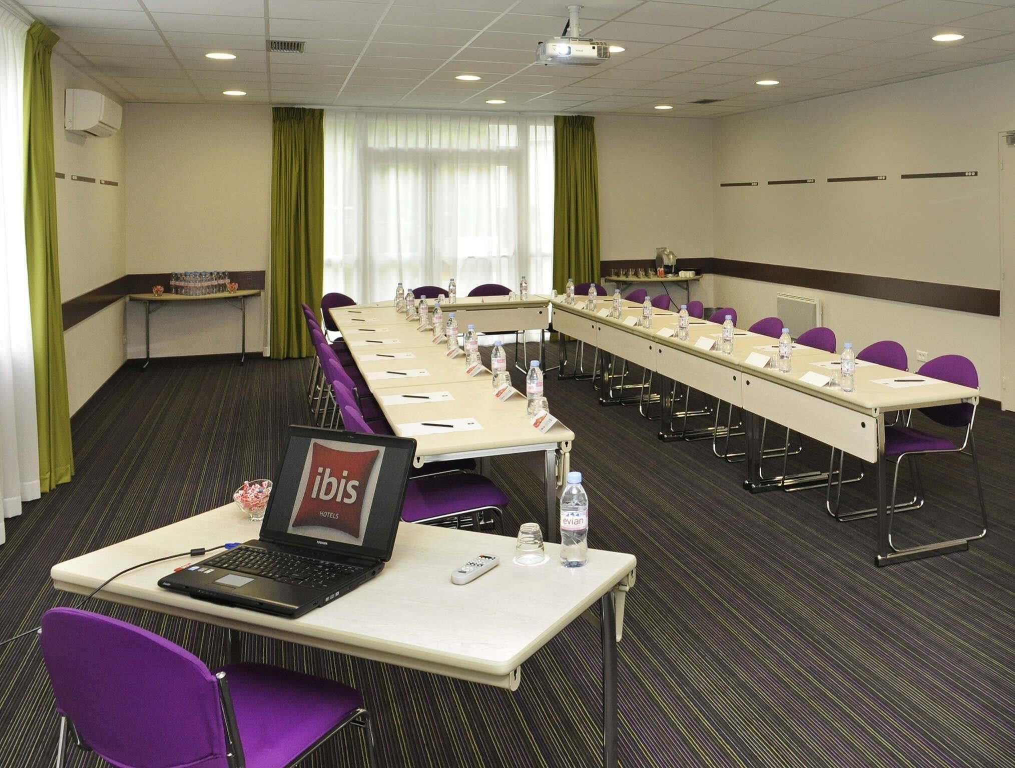 A conference room with a long table, purple chairs, a laptop, and water bottles.