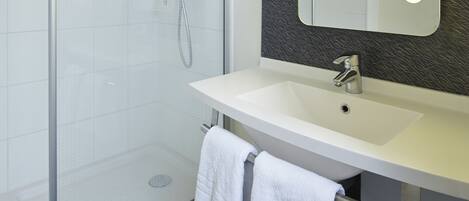 Une salle de bain moderne dotée d’une douche à parois de verre, d’un lavabo blanc et d’un grand miroir avec éclairage intégré.