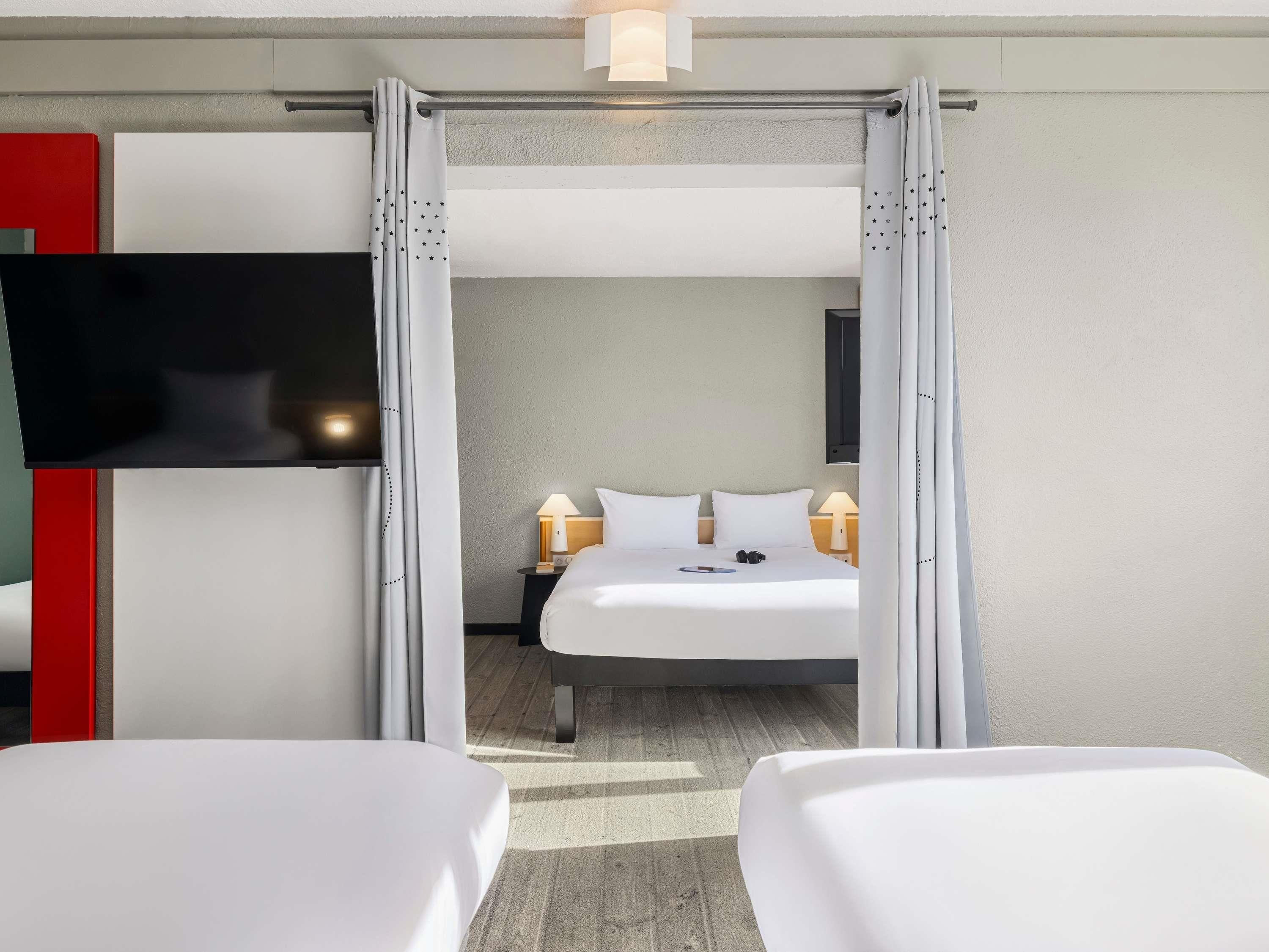 Une chambre d’hôtel avec un lit, un téléviseur fixé au mur et une table de chevet avec une lampe.