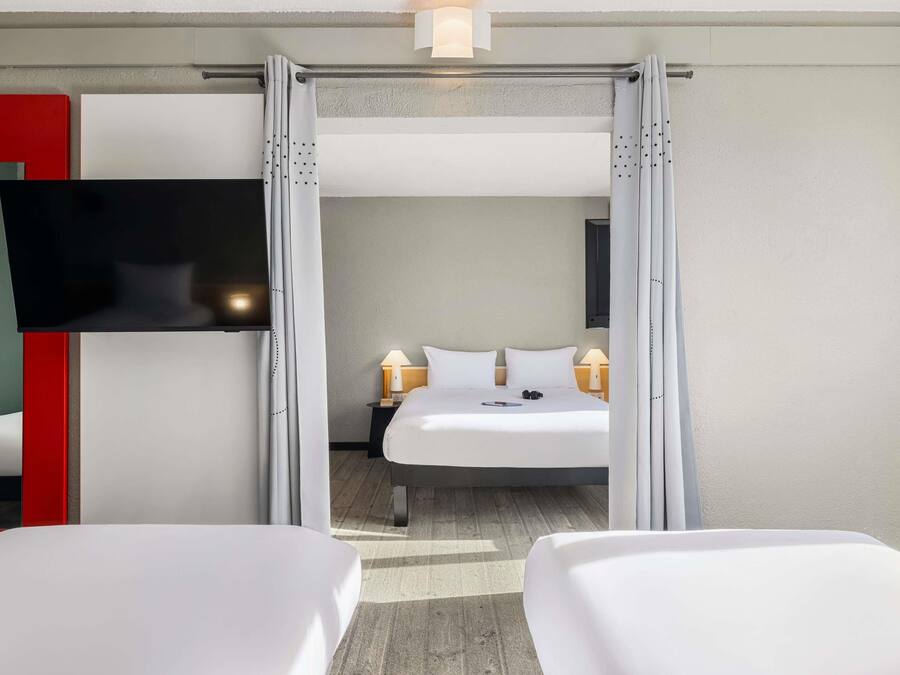 A hotel room with a bed, a TV mounted on the wall, and a nightstand with a lamp.