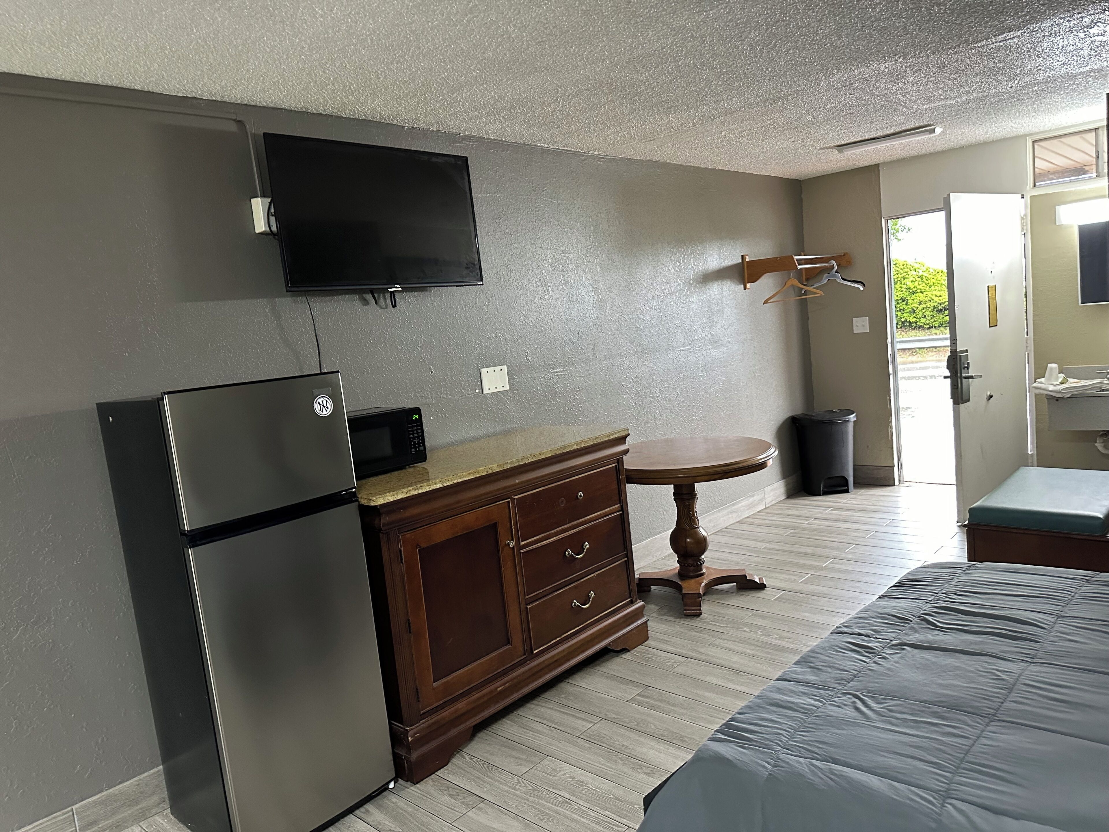 Una habitación compacta con refrigerador, microondas, cómoda de madera, mesa redonda y una cama.