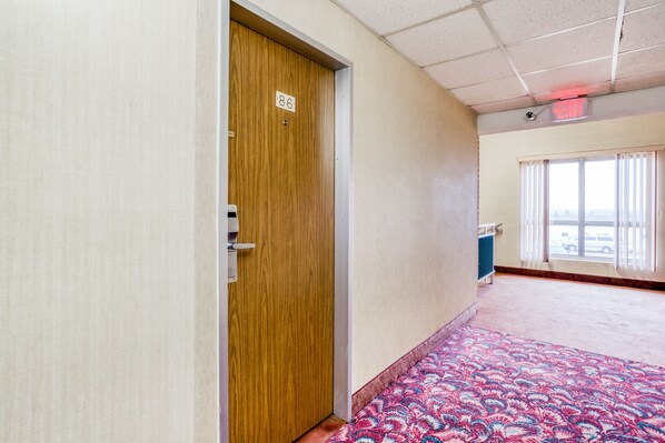 A hotel room with a wooden door marked 86, a patterned carpet, and a window with blinds. - Bravo Inn Greensboro (Greensboro)