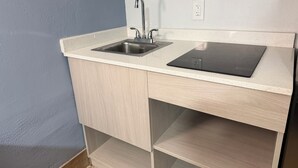 A kitchen with a stainless steel sink, a black induction cooktop, and light wood cabinetry. - Bravo Inn Greensboro (Greensboro)