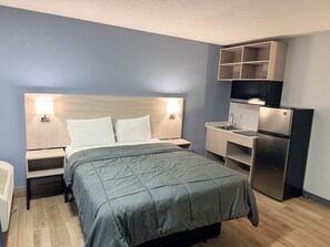 Habitación de hotel con cama, mesitas de noche, escritorio, refrigerador y estante empotrado para la televisión.