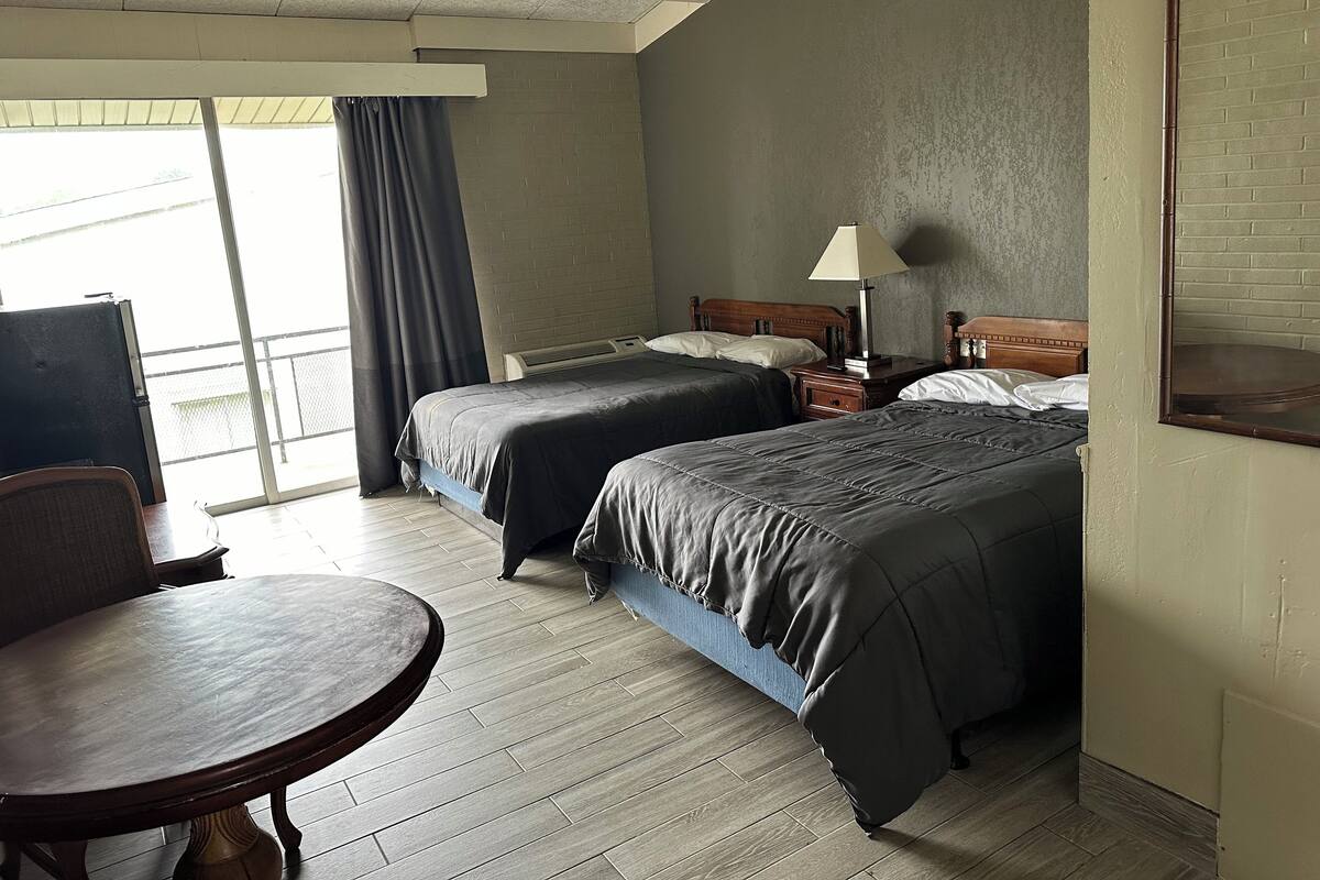 A hotel room with two beds, a table, and a chair.