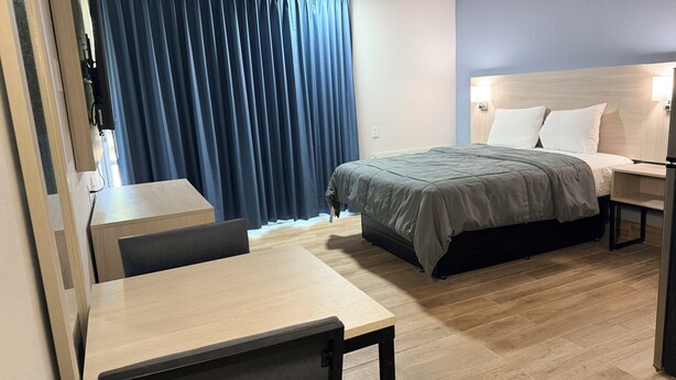 A hotel room with a bed, bedside table, desk, chair, and a window with curtains. - Bravo Inn Greensboro (Greensboro)