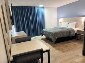 Habitación de hotel con cama, mesita de noche, escritorio, silla y ventana con cortinas.