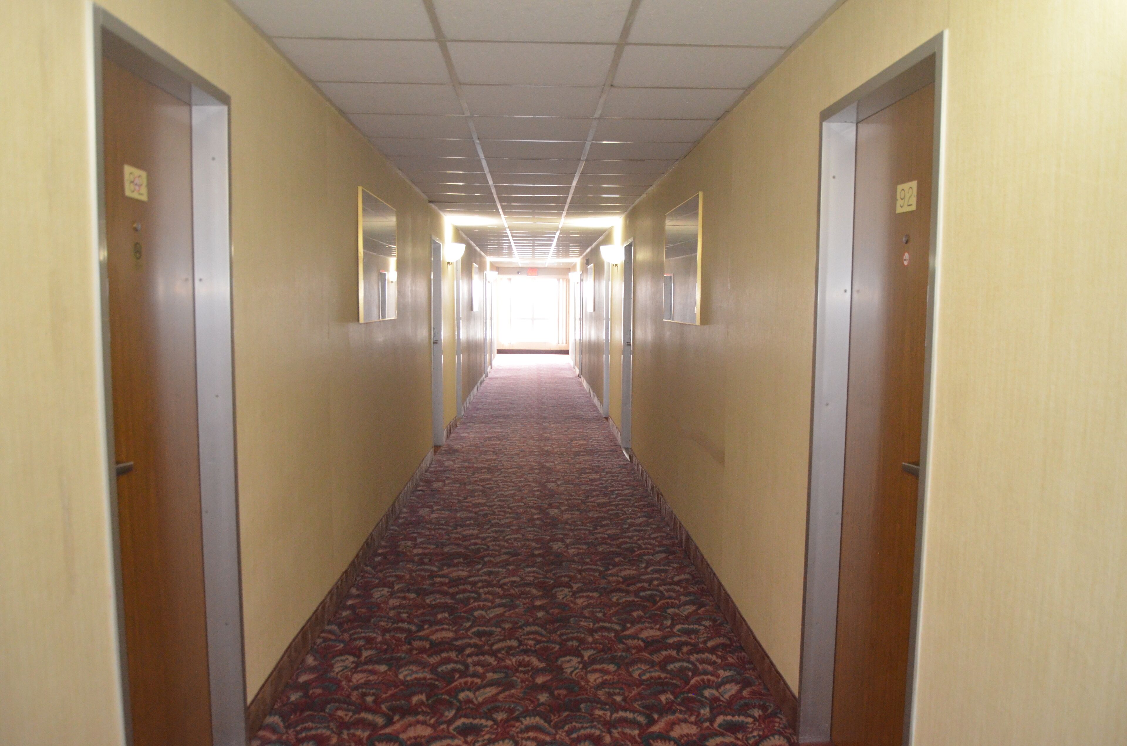 A long, narrow hallway with carpeted floors and doors on both sides, leading to an open area at the end.