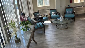 A spacious living room with a large window, a fireplace, and a comfortable seating area with chairs and a coffee table. - Bravo Inn Greensboro (Greensboro)