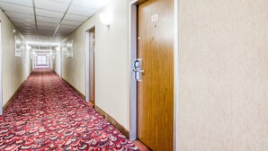 A hotel corridor with a patterned carpet, wooden doors, and a light fixture on the ceiling. - Bravo Inn Greensboro (Greensboro)