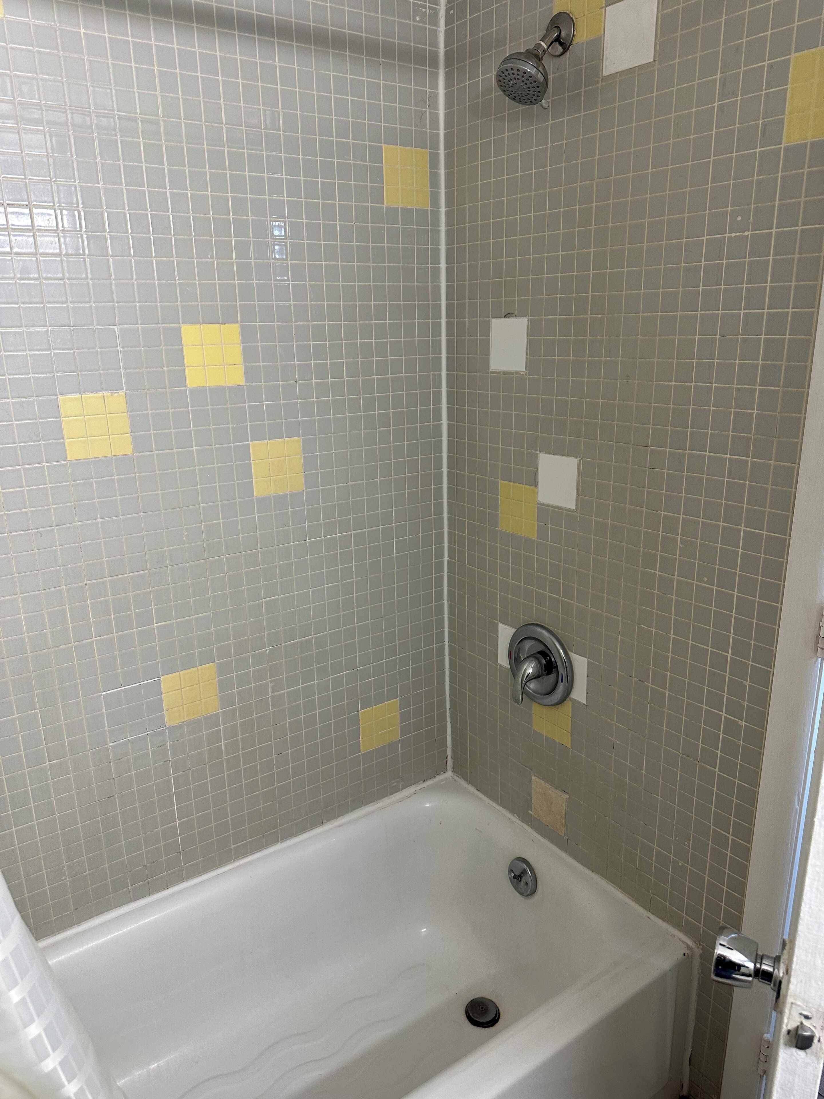 A bathroom with a white bathtub, a showerhead, and tiled walls with yellow squares.