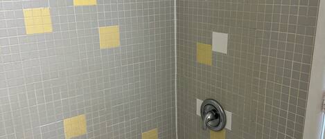 A bathroom with a white bathtub, a showerhead, and tiled walls with yellow squares.