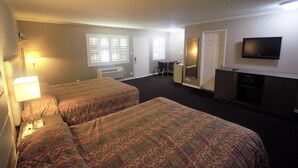 A hotel room with two beds, a desk, a television, and a window with blinds.