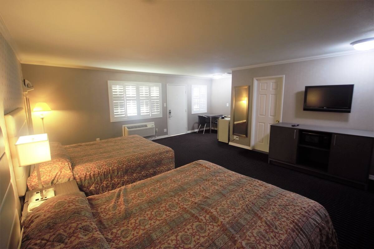 A hotel room with two beds, a desk, a television, and a window with blinds.