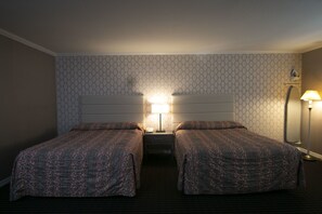 A hotel room with two beds, a nightstand, a lamp, and a patterned wall. - Alpha Inn & Suites (San Francisco)