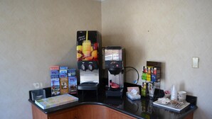 A self-service beverage station with a coffee machine and a fruit juice dispenser, along with various food items and condiments on the counter.